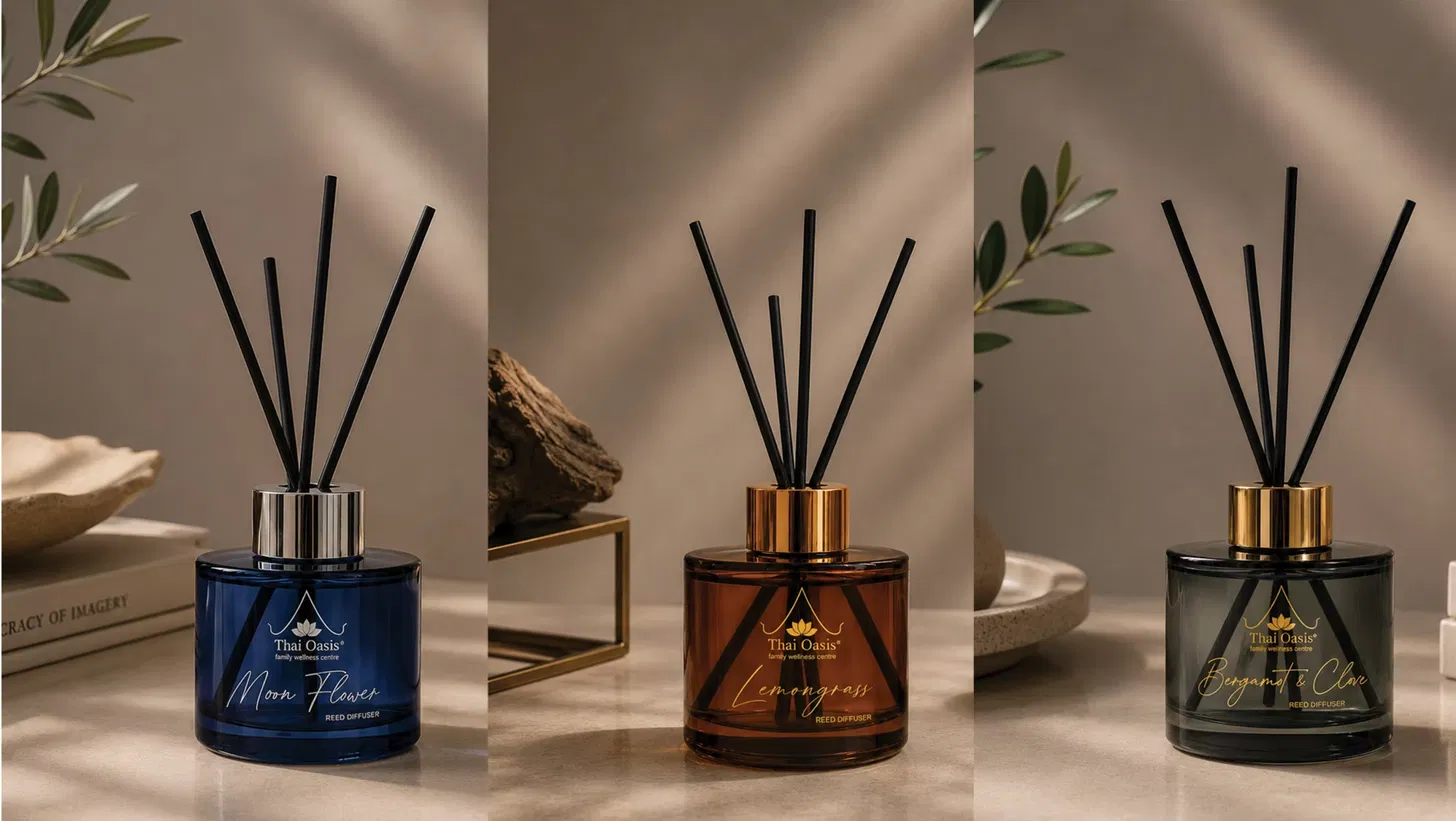 Three Thai Oasis reed diffusers in soft daylight — Moon Flower in deep blue glass, Lemongrass in amber glass, and Bergamot & Clove in smoked grey glass, each with black reeds